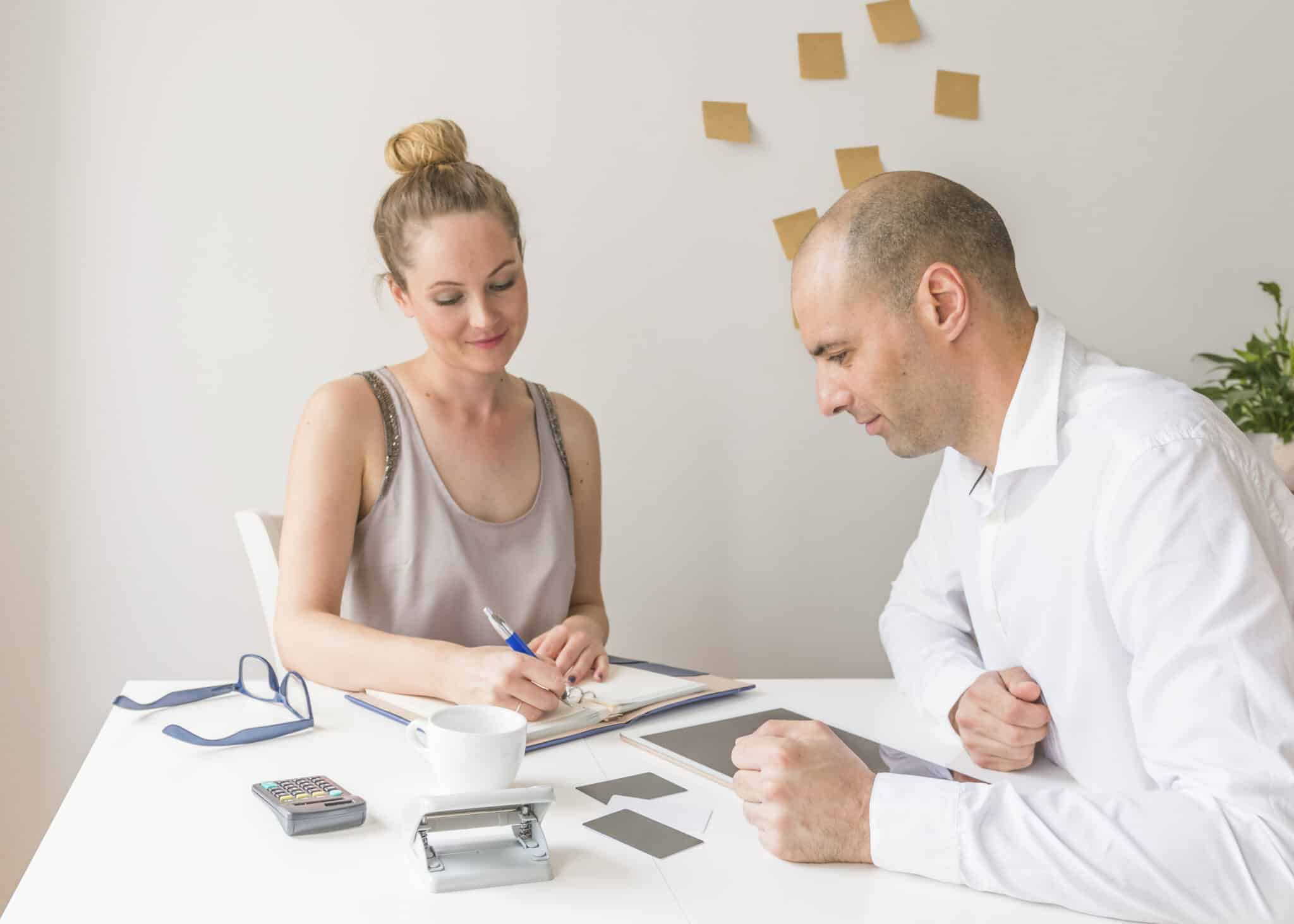 homme-affaires-regarder-femme-affaires-ecrire-journal-sur-lieu-de-travail-scaled
